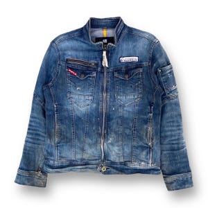 Puede incluir: Una chaqueta vaquera azul con cierre de cremallera, múltiples bolsillos y varios detalles desgastados. La chaqueta tiene una etiqueta con el texto "B.R.U.T.L.E." y otra etiqueta con el texto "International Co. Ltd."
