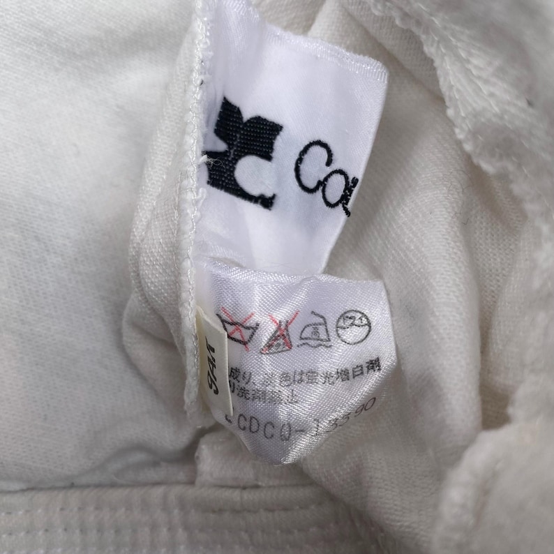 May include: White clothing tag with black text that reads "Car" and a black logo. The tag also has a white care label with Japanese text and symbols for washing instructions. The text "_CDCO_ - 155/90" is also visible.