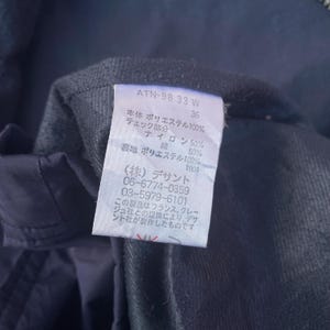 May include: Close-up of a garment tag with Japanese text and the code ATN-98 33 W. The tag also lists fabric composition: 100% polyester, 50% nylon, and 50% cotton. The tag is white with black text.