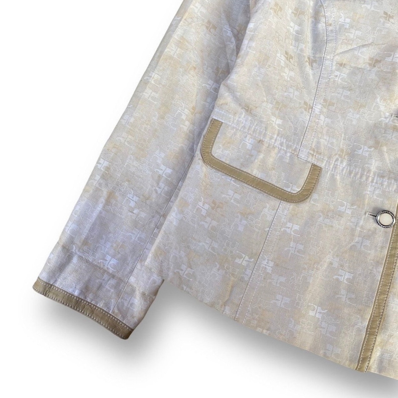 May include: A beige blazer with a white patterned design and brown trim. The blazer has a single button closure and a pocket on the left side.