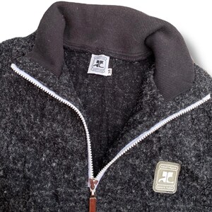 K&ouml;nnte beinhalten: Dunkelgraue Jacke mit Rei&szlig;verschluss, schwarzem Kragen und wei&szlig;em Rei&szlig;verschluss. Die Jacke hat einen kleinen Logoaufn&auml;her und ein Etikett mit dem Text "courr&egrave;ges sport futur".