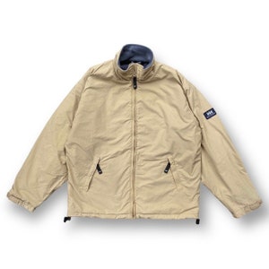 Puede incluir: Una chaqueta beige forrada de polar con cierre de cremallera y un parche con el logotipo HH negro en la manga derecha.