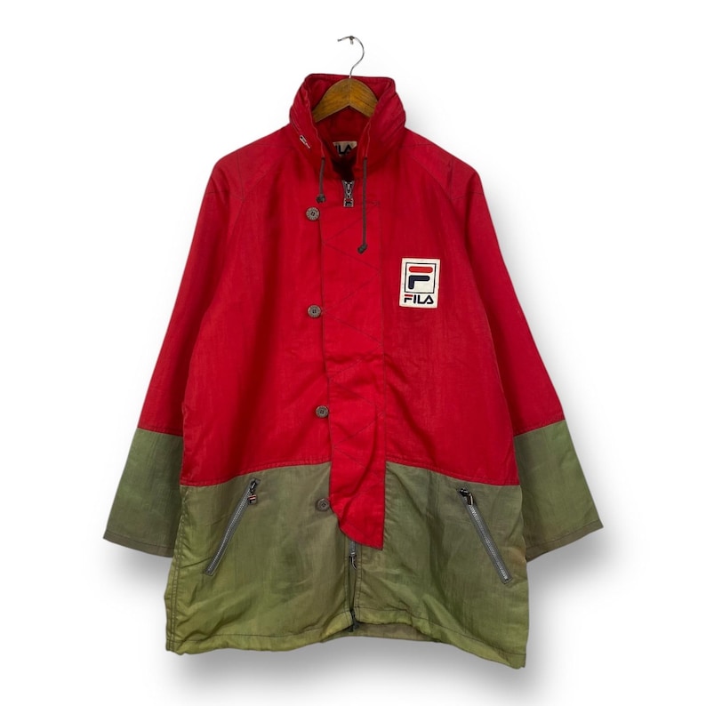 Op de afbeelding: Rood en groen vintage Fila jack met een groot Fila logo op de borst. Het jack heeft een rits en knoopsluiting.
