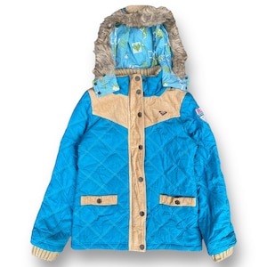 Puede incluir: Una chaqueta acolchada azul con un panel de pana marrón y una capucha forrada de piel sintética. La chaqueta tiene una cremallera y botones decorativos. La chaqueta tiene un parche de logotipo en la manga izquierda que dice "Roxy".