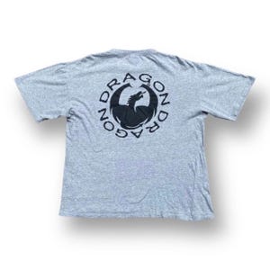 May include: A grey t-shirt with a black dragon logo on the back. The logo is a circle with the word "Dragon" written around it.