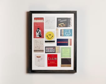 May include: A framed collage of matchboxes with various designs, including a smiley face, a couple, and a cityscape. The matchboxes are arranged in a grid pattern and have a black frame.