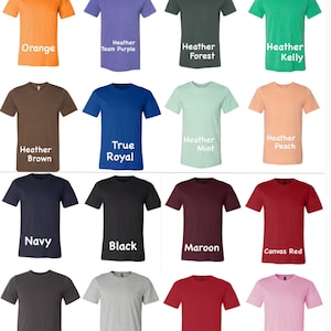 K&ouml;nnte beinhalten: Eine Sammlung von einundzwanzig einfarbigen T-Shirts in verschiedenen Farbt&ouml;nen, darunter Lila, Gr&uuml;n, Orange, Blau, Braun, Schwarz, Rot und Rosa. Jedes Shirt hat einen Rundhalsausschnitt und kurze &Auml;rmel. Die Farbbezeichnungen sind in wei&szlig;em Text dargestellt.