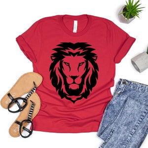 K&ouml;nnte beinhalten: Ein rotes T-Shirt mit einem schwarzen L&ouml;wenkopf-Design. Das Shirt wird mit Sandalen, einer Jeans und kleinen Topfpflanzen pr&auml;sentiert. Die L&ouml;wen-Grafik ist auf dem Shirt zentriert, mit einer detaillierten, stilisierten M&auml;hne und Gesichtsz&uuml;gen.