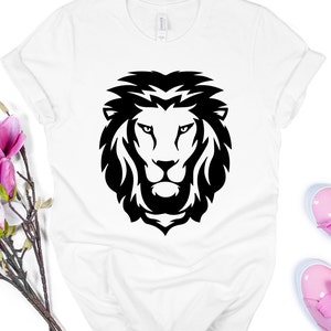 K&ouml;nnte beinhalten: Wei&szlig;es T-Shirt mit einem auff&auml;lligen schwarzen L&ouml;wenkopf-Design. Das Gesicht des L&ouml;wen ist mit einer detaillierten M&auml;hne und scharfen Linien dargestellt. Das Shirt besteht aus einem weichen Material und hat hochgekrempelte &Auml;rmel.