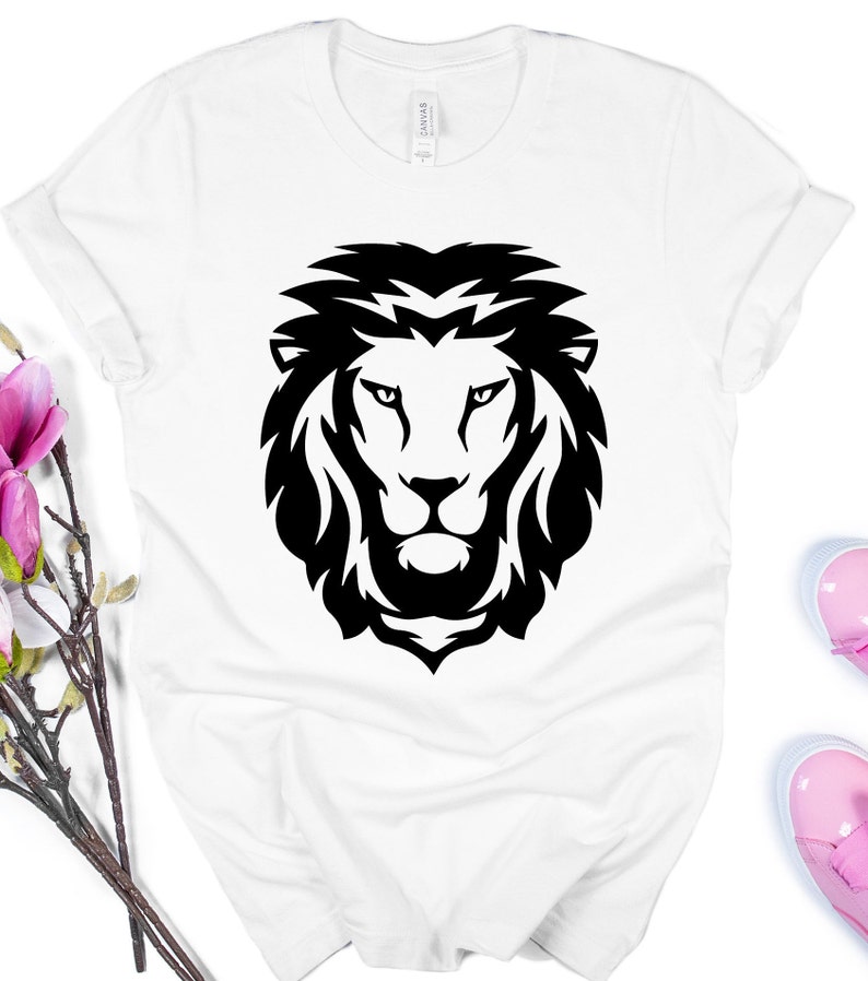 K&ouml;nnte beinhalten: Wei&szlig;es T-Shirt mit einem auff&auml;lligen schwarzen L&ouml;wenkopf-Design. Das Gesicht des L&ouml;wen ist mit einer detaillierten M&auml;hne und scharfen Linien dargestellt. Das Shirt besteht aus einem weichen Material und hat hochgekrempelte &Auml;rmel.