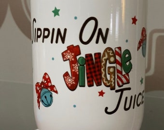 以下が含まれることがあります： 「Sippin' On Jingle Juice」と書かれた、赤、緑、白のデザインが施された白いセラミックタンブラーです。