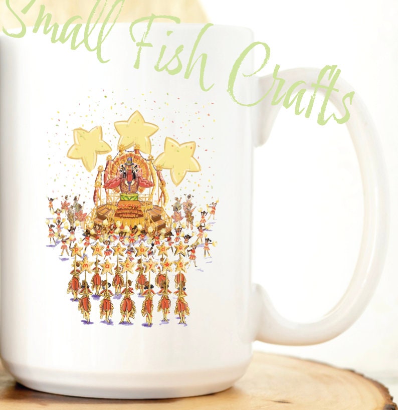 Pu&ograve; includere: Una tazza in ceramica bianca con un'illustrazione colorata di una parata con un grande carro e molte persone che marciano. Il carro ha tre grandi stelle gialle in cima. Il testo "Small Fish Crafts" &egrave; scritto in corsivo verde nell'angolo in alto a destra della tazza.