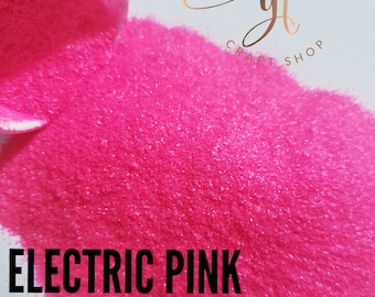 May include: A close-up of a bright pink glitter, with the text "ELECTRIC PINK" in black letters at the bottom of the image. The glitter is being poured from a container, and the text "GLITTERZ BY TRAECI CRAFT SHOP" is visible in the top right corner of the image.