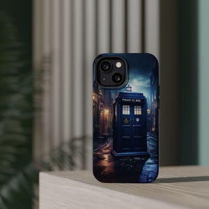May include: A smartphone case featuring a dark, atmospheric graphic of a blue police box standing on a wet, cobblestone street at night. The box has illuminated windows and the text POLICE BOX printed clearly above the double doors.