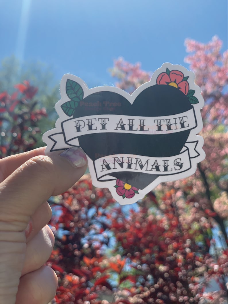 May include: A black heart-shaped sticker with the text "PET ALL THE ANIMALS" in white lettering. The sticker has a white banner with a red flower on each side.