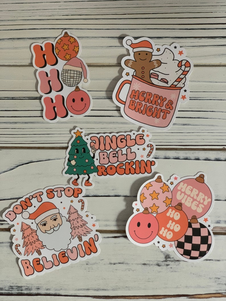 May include: Set of five Christmas-themed stickers featuring illustrations of Santa Claus, a gingerbread man, a Christmas tree, and ornaments. The stickers have a retro, vintage aesthetic with pink, orange, and white colors. The text on the stickers includes "Ho Ho Ho", "Merry & Bright", "Jingle Bell Rockin", "Don't Stop Believin", and "Merry Vibes".