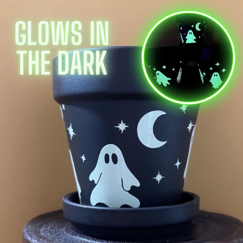 May include: Black terracotta planter with a glow-in-the-dark design featuring white ghosts, moons, and stars.  The text "GLOWS IN THE DARK" is visible in the top left corner of the image.