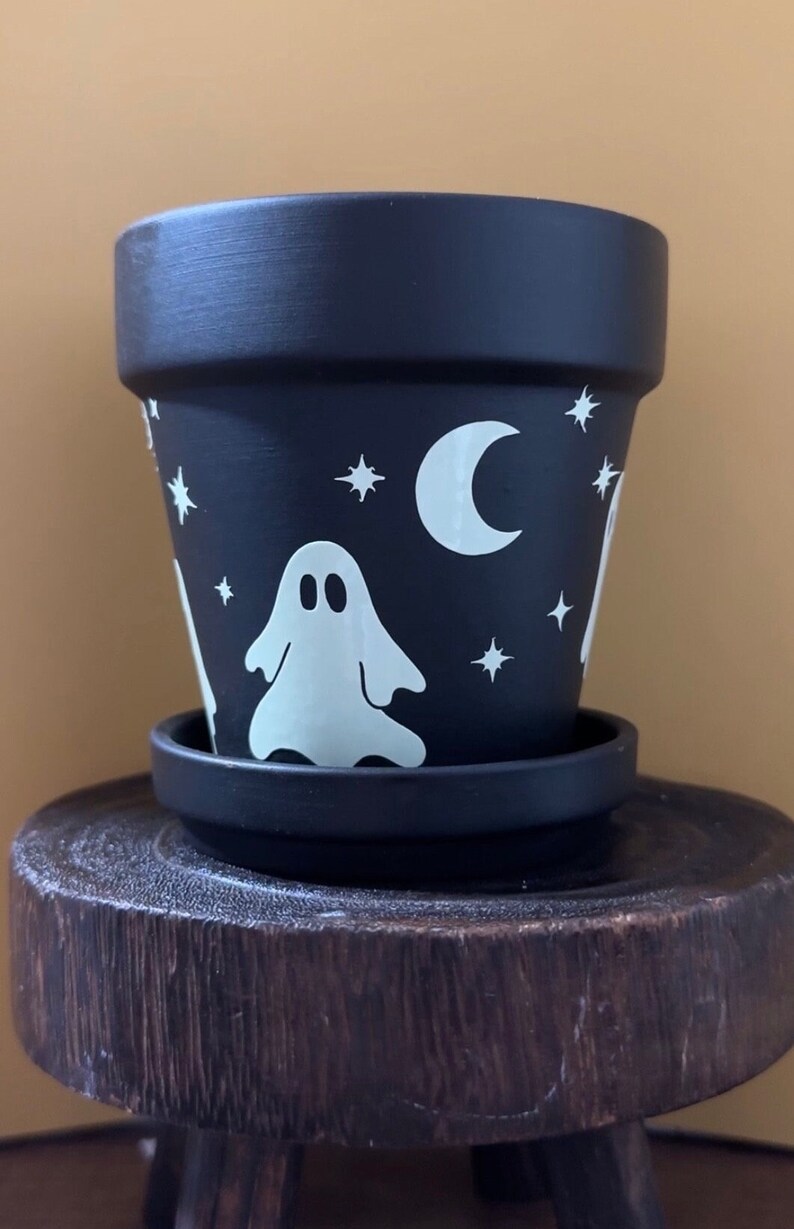 May include: Black terracotta planter with a white ghost, crescent moon, and stars design. The planter has a matching saucer.
