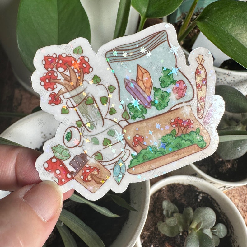 May include: A holographic sticker featuring a variety of whimsical illustrations, including a glass bong, a bag of marijuana, a joint, mushrooms, and crystals. The sticker has a sparkly, iridescent finish.