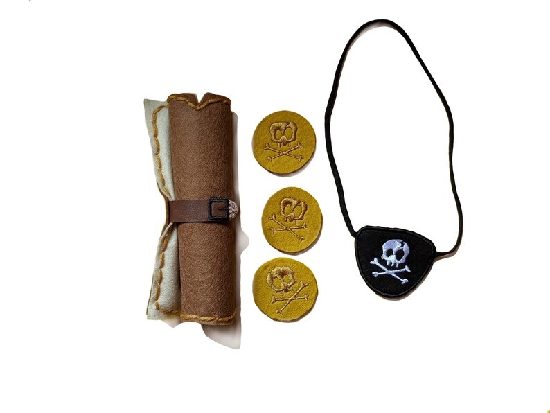 May include: A pirate-themed play set featuring a rolled-up brown felt scroll secured with a brown belt, three gold-colored coins with skull and crossbones, and a black eye patch with a skull and crossbones design.