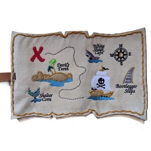 May include: A beige felt pirate map with embroidered details. Features a red "X" marking treasure, a pirate ship, and landmarks like "Devil's Teeth" and "Bootlegger Steps." Includes a brown leather strap.