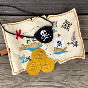 Pode incluir: Um conjunto de jogos com tema pirata em feltro com um mapa com detalhes bordados, incluindo um tapa-olho com caveira e ossos cruzados, uma bússola e um navio pirata. Inclui três fichas de moedas de ouro com desenhos de caveiras.