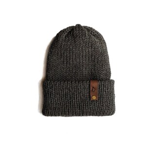 May include: A gray knitted beanie with a brown leather patch that says "Camp" on it.