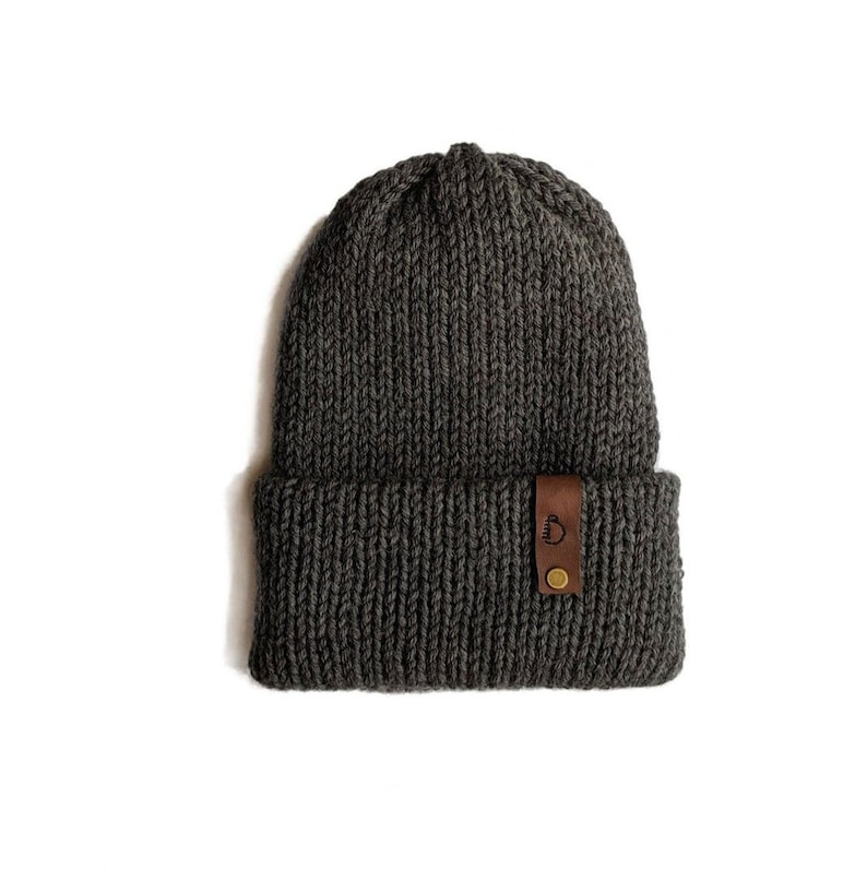 May include: A gray knitted beanie with a brown leather patch that says "Camp" on it.