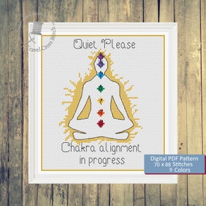 May include: Cross stitch pattern featuring a white silhouette of a person in a yoga pose with seven colorful chakras. The text "Quiet Please" is at the top and "Chakra alignment in progress" is at the bottom. The pattern is 70 x 88 stitches and uses 9 colors.