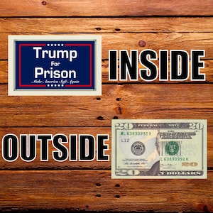以下が含まれることがあります： 木製の背景にテキストが配置された画像です。「Trump For Prison」というテキストが青と赤のフレームで囲まれ、「INSIDE」と「OUTSIDE」の文字、20ドル紙幣が描かれています。