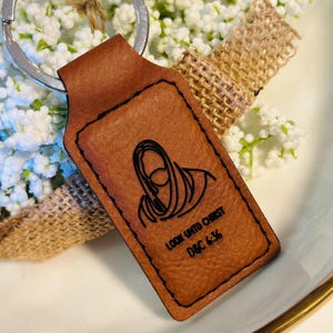 May include: Brown leather keychain with a rectangular tag featuring a black silhouette of a person with the text "LOOK UNTO CHRIST D&C 6:36"