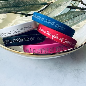 May include: Five silicone wristbands with the text "Disciple of Jesus Christ" in black lettering. The wristbands are in the colors blue, white, black, pink, and red.