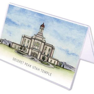 May include: A watercolor illustration of the Deseret Peak Utah Temple, a white building with a brown roof and a tall spire. The temple is surrounded by green trees and grass, and the sky is blue with white clouds. The text "Deseret Peak Utah Temple" is printed below the image.