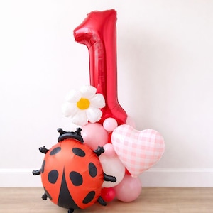 Puede incluir: Un arreglo festivo de globos para un primer cumpleaños. Presenta un gran globo rojo con el número 1, un globo de mariquita, un globo de margarita blanca, un globo de corazón rosa y varios globos rosas más pequeños.