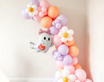 May include: A balloon arch featuring a mix of pastel pink, orange, and lavender balloons. The arrangement includes white daisy-shaped balloon flowers with yellow centres and a foil ghost balloon wearing a pink bow and holding a pumpkin.