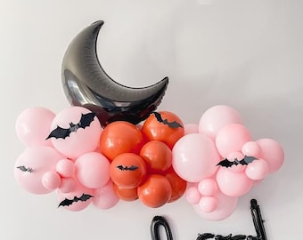 Peut inclure: Une guirlande de ballons noirs et roses avec un ballon en forme de croissant de lune noir et des découpes de chauves-souris noires. La guirlande épelle "boo!" en ballons noirs.