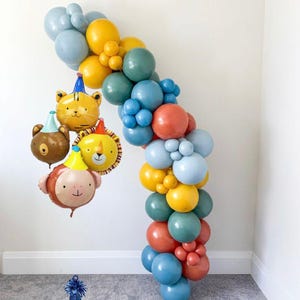 May include: A vibrant balloon garland in blue, yellow, teal, and orange, with animal-shaped foil balloons. The balloons are arranged in an arch, suitable for a party. The animal balloons include a tiger, bear, lion, and monkey, all wearing party hats.