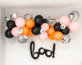 Peut inclure: Une guirlande de ballons d'Halloween avec des ballons noirs, orange et roses. Les ballons ont différents motifs, notamment des chauves-souris, des crânes et du marbre. La guirlande est décorée du mot "boo!" en ballons noirs.