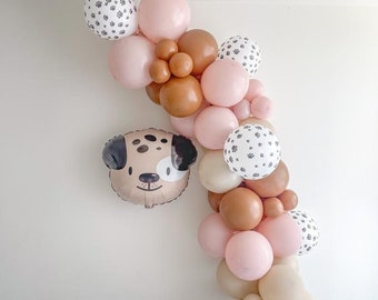 May include: A balloon arch made of pink, brown, and white balloons. The balloons have a paw print pattern. A brown and white dog balloon is attached to the arch.