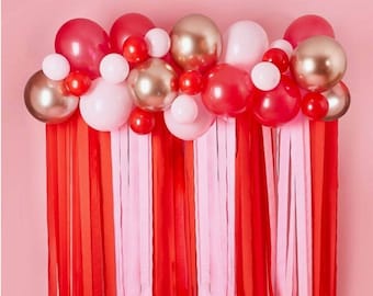 May include: A red and pink balloon garland with streamers hanging down. The balloons are a mix of metallic and matte finishes.