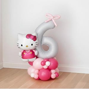 May include: A festive balloon arrangement featuring a Hello Kitty character balloon and a silver number six balloon. The base is composed of pink and white balloons. A pink bow adorns the top of the number six balloon. Perfect for a birthday celebration.