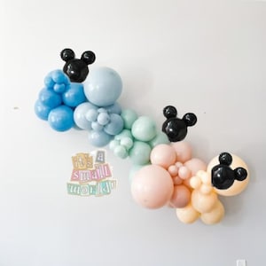 May include: A balloon garland featuring pastel blue, green, and peach balloons. The garland is decorated with black Mickey Mouse ears. The text "it's a small world" is visible in the image.