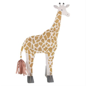 May include: A cardboard cutout of a giraffe with a pink tassel tail. The giraffe is brown with a white background and a black outline. The giraffe is standing on a white background.