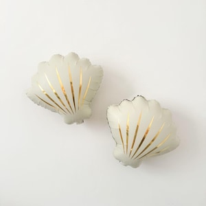 May include: Two seashell-shaped balloons in a pale, off-white hue, adorned with gold vertical stripes. The balloons are set against a plain white backdrop, offering a minimalist design. Ideal for a beach or nautical themed event.