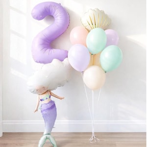 Może przedstawiać: Zestaw balonów w pastelowych kolorach, w tym duży balon w kształcie cyfry 2, balon w kształcie muszli i balon w kształcie syreny. Balon syreny ma fioletowy ogon i białą głowę w kształcie chmury. Dekoracja urodzinowa.