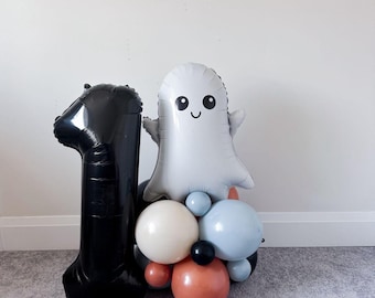 Può includere: Un palloncino nero a forma di numero uno e un palloncino bianco a forma di fantasma con una faccia sorridente. I palloncini fanno parte di un'arrangiamento decorativo con vari palloncini rotondi bianchi, blu, neri e arancioni.