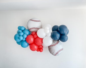 May include: A garland of blue, red, and white balloons with baseball-themed balloons. The baseball balloons are white with red stitching.