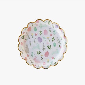 May include: White paper party plates with a gold scalloped edge. The plates feature a repeating pattern of pastel coloured eggs, bunnies, and flowers.