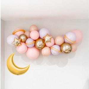 May include: A balloon garland with pink, lavender, and gold balloons in the shape of planets and stars. A gold crescent moon balloon is on the left side of the image.
