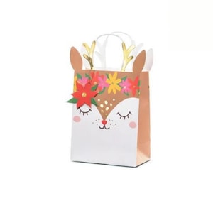 Könnte beinhalten: Eine braune und weiße Geschenktüte mit einem Rentiergesicht und einem Blumenkranz. Das Rentier hat geschlossene Augen und eine kleine rote Blume an der Seite des Kopfes.